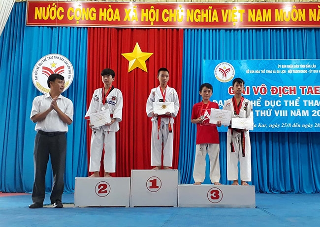 Em Phùng Quang Huy (giữa) nhận Huy chương Vàng tại Giải vô địch Taekwondo,  Đại hội Thể dục Thể thao tỉnh Đắk Lắk lần thứ VIII, năm 2017-2018.  