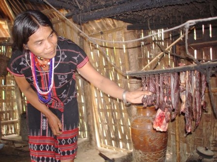 Phụ nữ Cơ Tu kiểm tra món thịt xông trên giàn bếp.