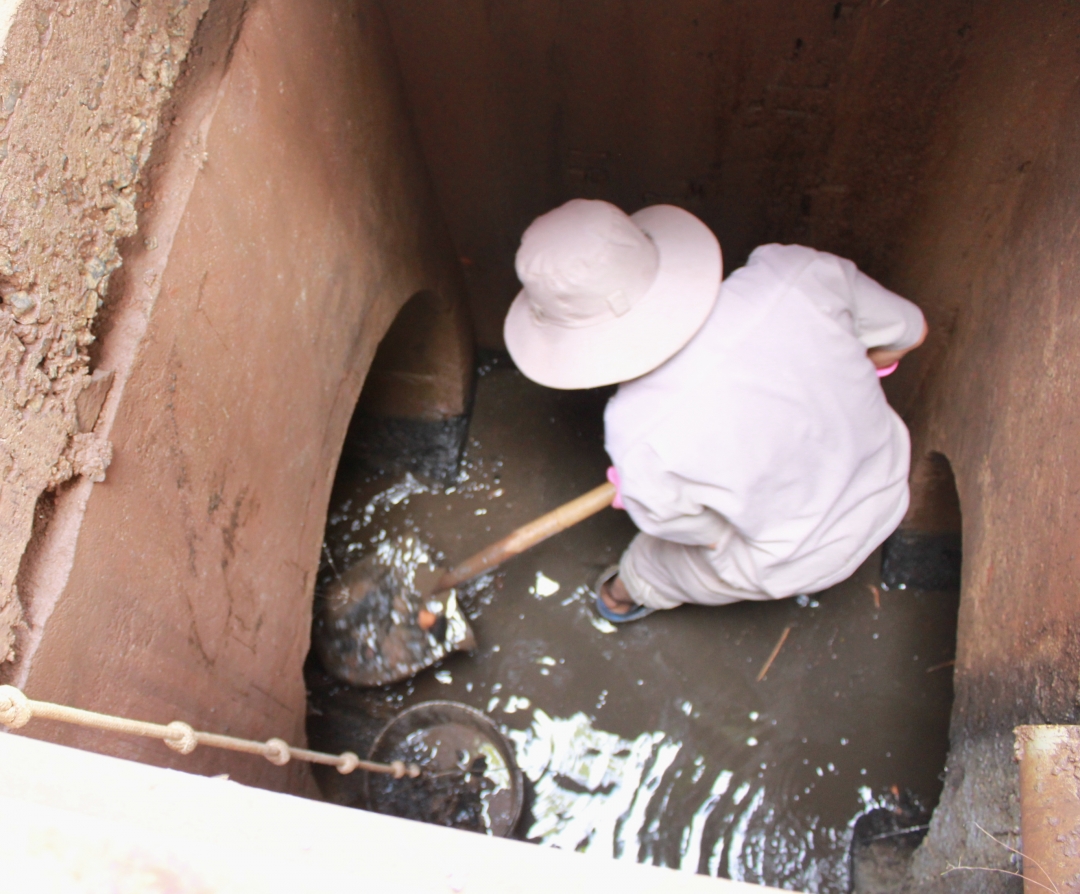 Dưới hố ga, anh Trương Quang Đắc phải khom người, dùng xẻng chui hẳn vào lòng ống cống để xúc bùn và rác cho vào xô