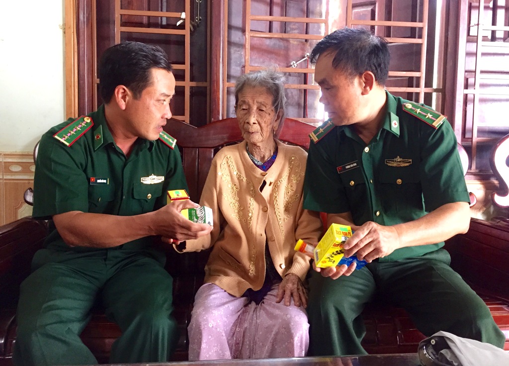 Cán bộ quân y Đồn Biên phòng Cửa khẩu Đắk Ruê tận tình thăm hỏi sức khỏe Mẹ Việt Nam Anh hùng Dương Thị Liễu. Ảnh: Quân Tùng