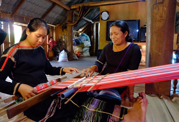 Chị H'Yam Bkrông (bên phải) hướng dẫn kỹ thuật dệt cho con em của xã viên. 