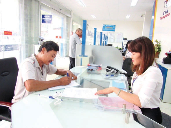 Khách hàng (bìa trái) làm thủ tục thanh toán tiền điện qua ngân hàng tại Điện lực Nam Buôn Ma Thuột.