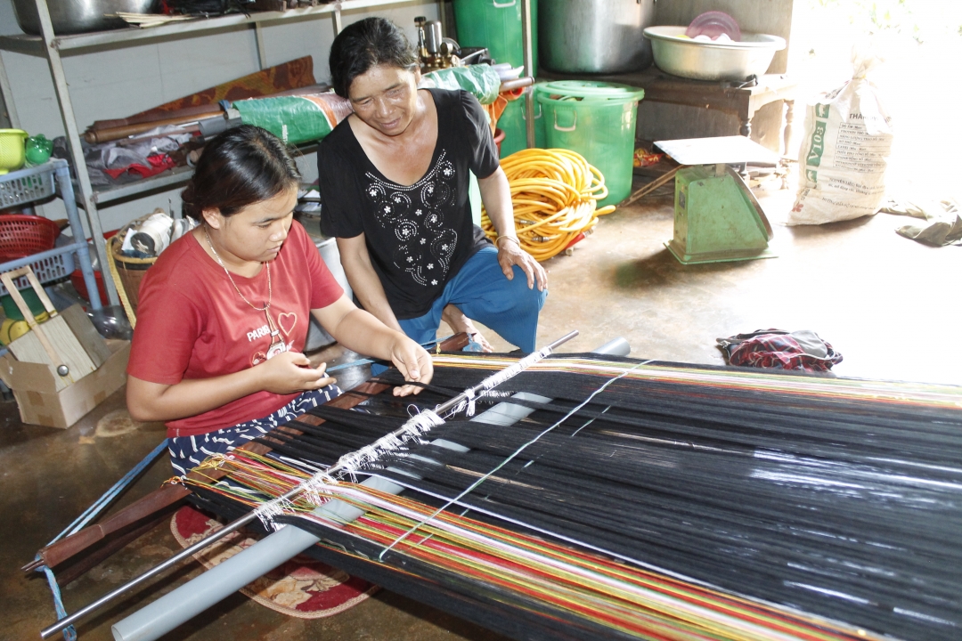 Bà H'Bin chỉ dạy H'Roanh cách dệt những tấm khăn và váy áo. 