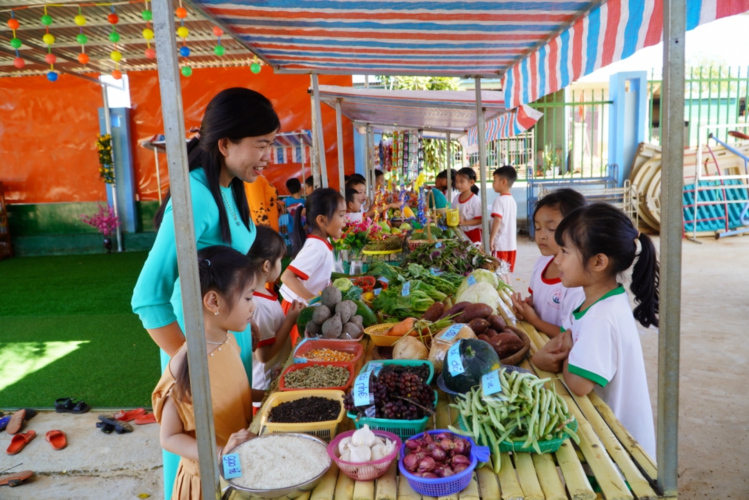 Cô và trò Trường Mầm non Ea Nam (xã Ea Nam) hào hứng tham gia phiên chợ quê tại sân trường. 